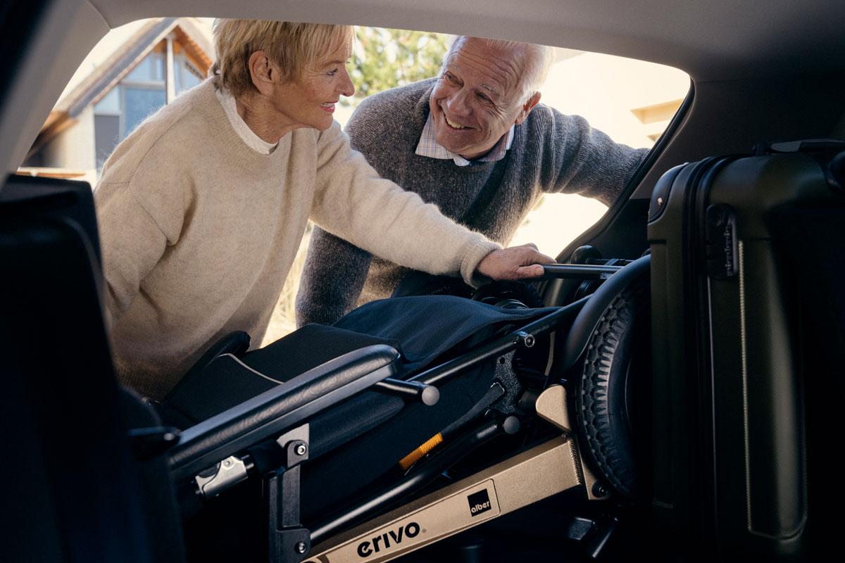 Mann und Frau verstauen zusammengefalteten erivo Elektrorollstuhl im Kofferraum ihres Autos.