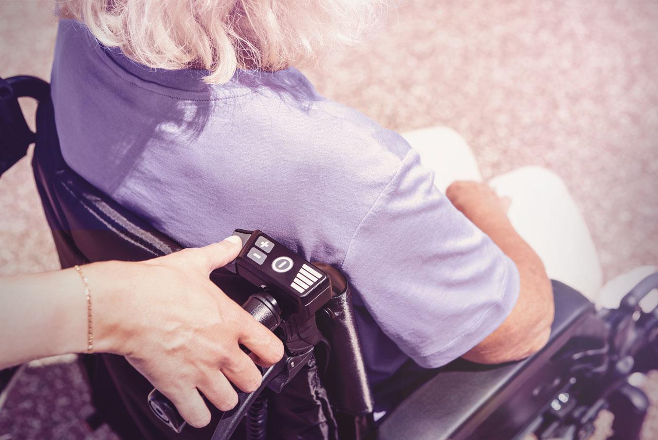 Frau im Rollstuhl mit via go, Hand der Begleitperson an Bedienelement.