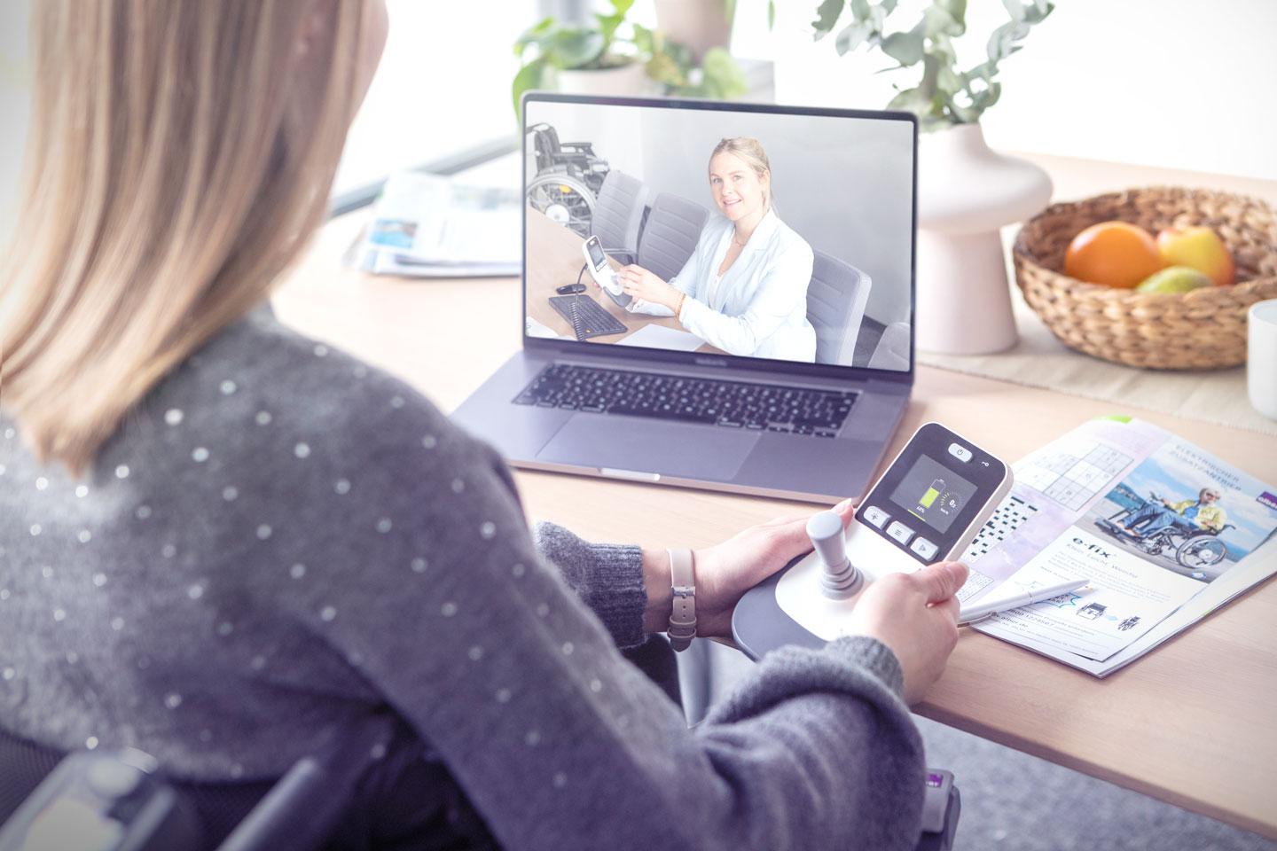 Frau mit e-fix Bediengerät in der Hand sitzt vor Laptop im Videocall mit Alber-Mitarbeiterin
