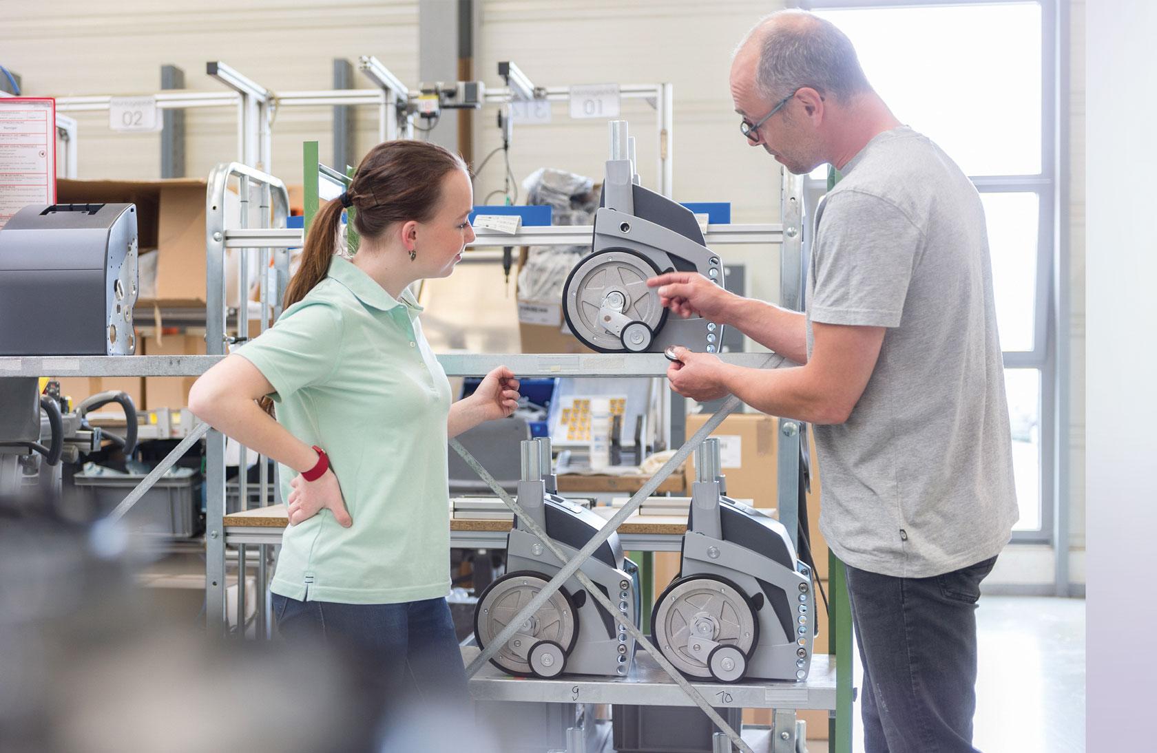 Einer Auszubildenden werden von ihrem Ausbilder in der Fertigung die technischen Features eines Alber-Produkts erklärt.