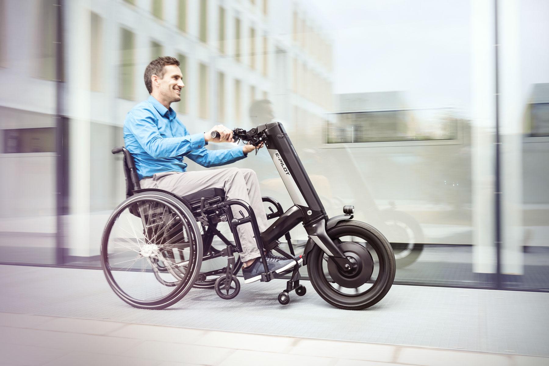 Mann in Rollstuhl mit elektrischem  Zusatzantrieb e-pilot auf dem Weg durch die Stadt.