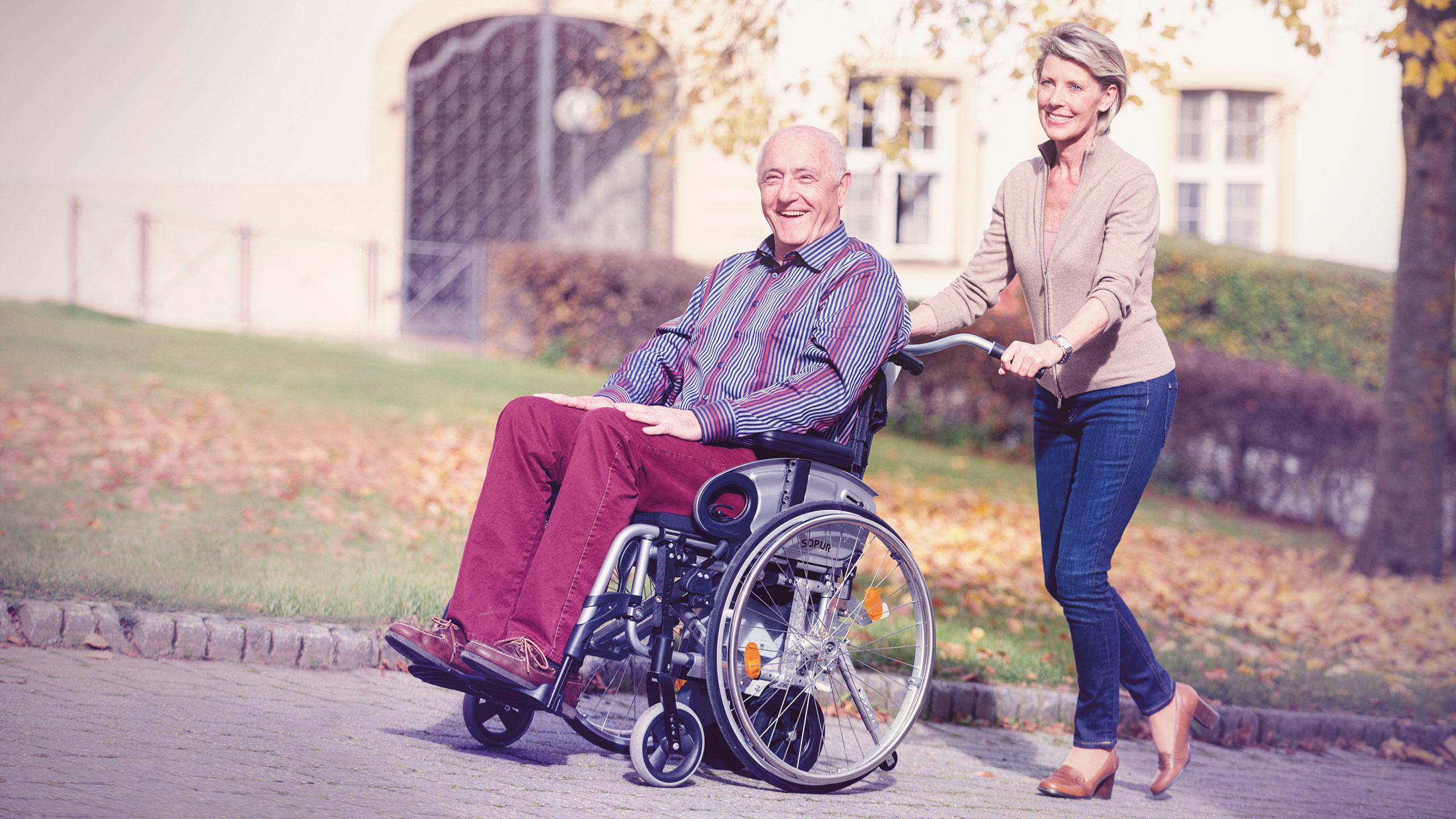 Frau schiebt Mann im Rollstuhl mit viamobil eco eine Steigung hinauf.