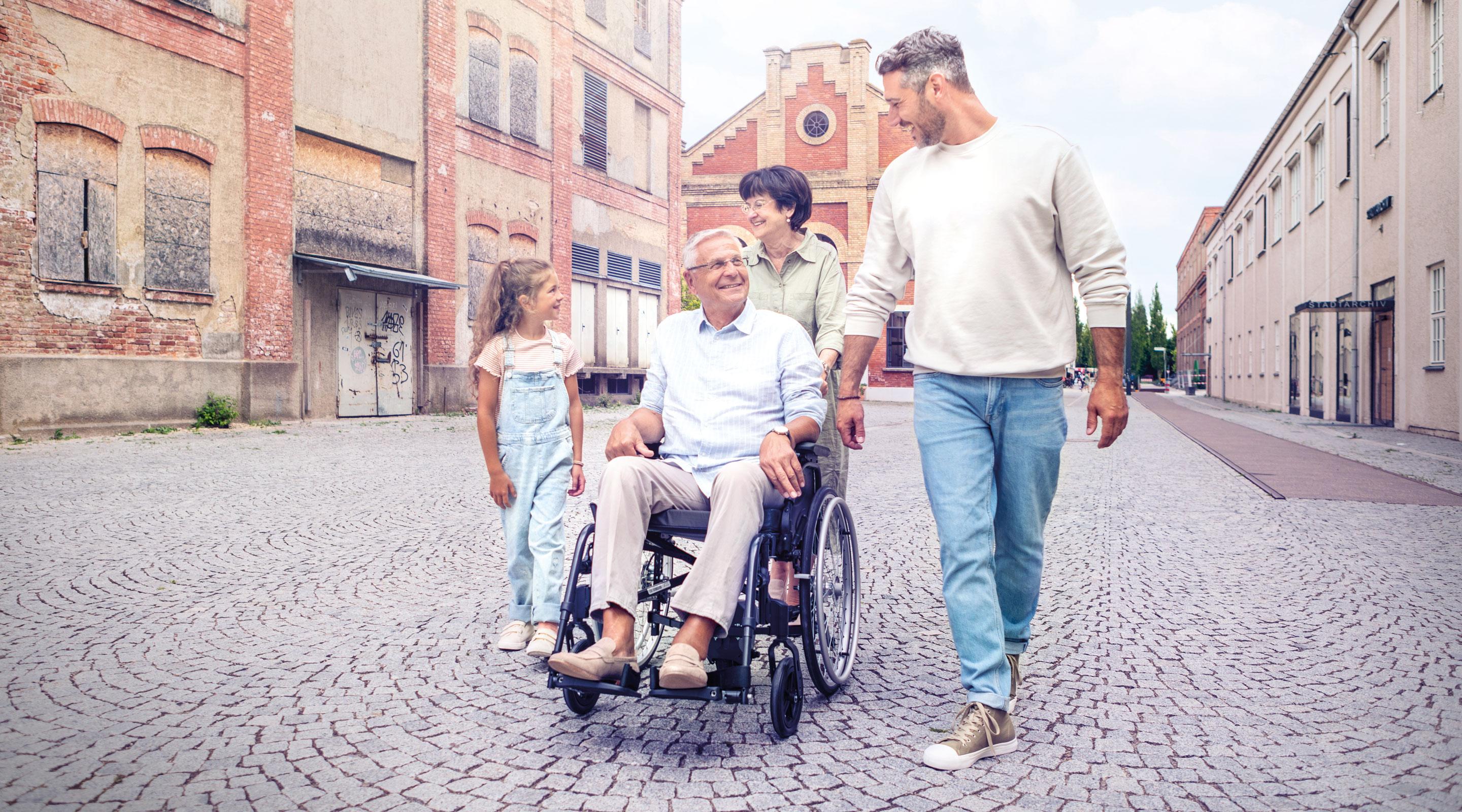 Familienausflug in der Stadt, Mann wird im Rollstuhl mit via go Schiebehilfe geschoben.