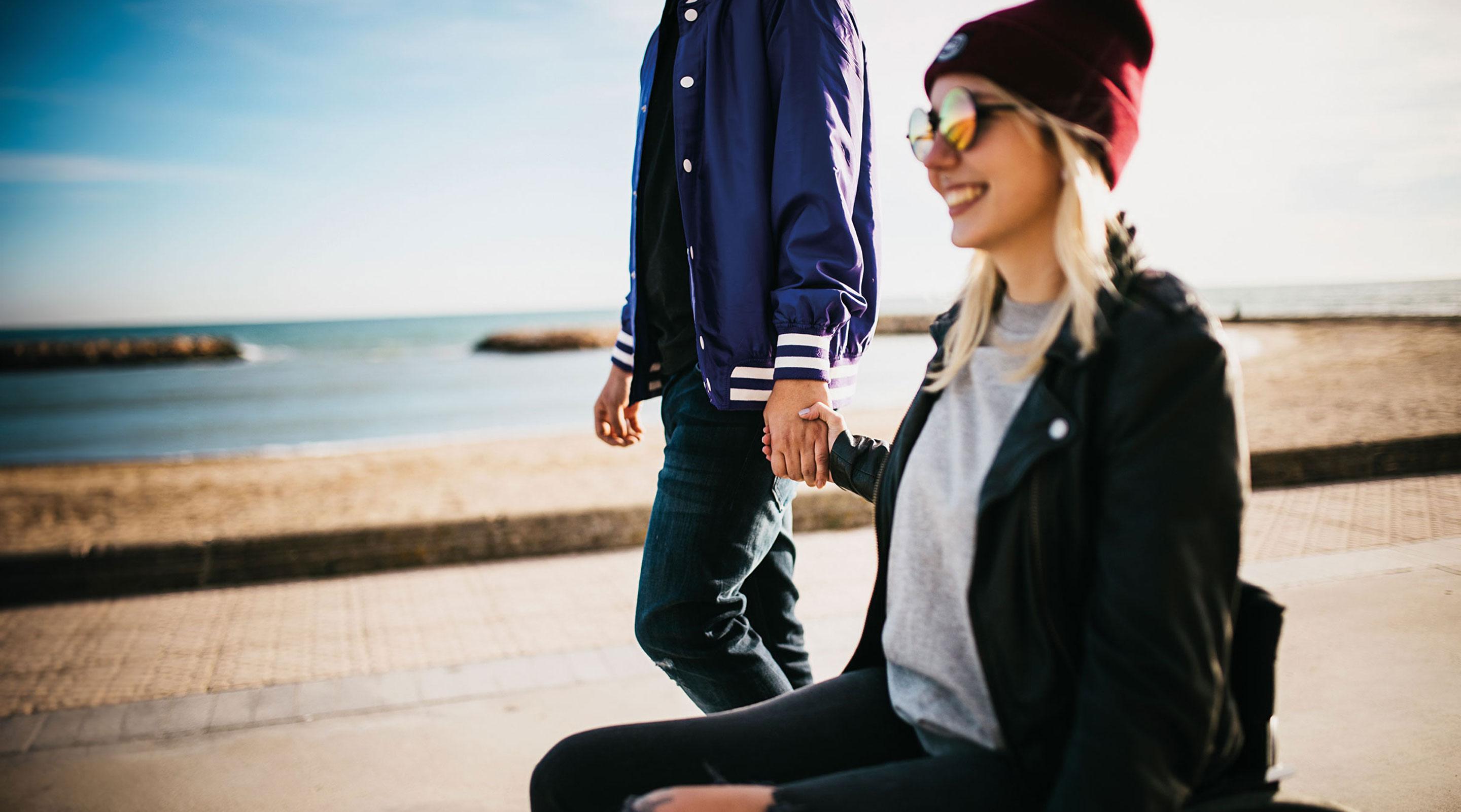 Junge Frau im Aktivrollstuhl mit smoov Zusatzantrieb fährt Hand in Hand mit ihrem Freund an der Strandpromenade.
