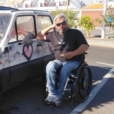 e-motion Nutzer K.D. Herzog sitzt in Rollstuhl und lehnt an altem Kleinwagen auf Teneriffa