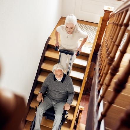 Eine Frau befördert ihren Mann mit dem Scalamobil die Treppe hinunter.