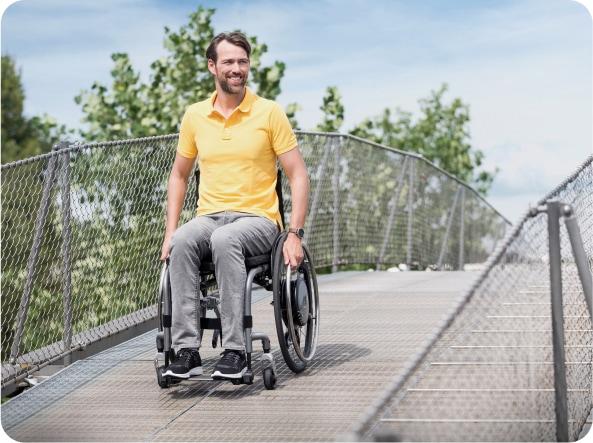 Mann im Rollstuhl mit kraftverstärkendem Antrieb e-motion fährt eine Fußgängerbrücke hinunter