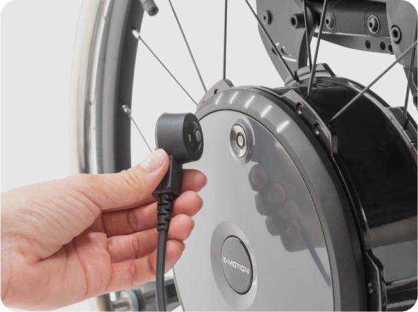 Hand hält EasyConnex Stecker an Ladebuchse von e-motion Radnabe zum Aufladen mit dem Automatik-Ladegerät