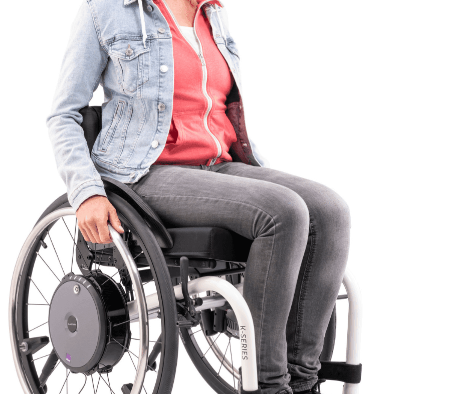 Eine Frau in einer Jeansjacke sitzt im Rollstuhl mit den Händen auf den Rädern
