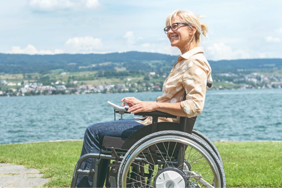 Frau in Rollstuhl mit e-fix Elektroantrieb macht Pause und genießt die Sonne am See