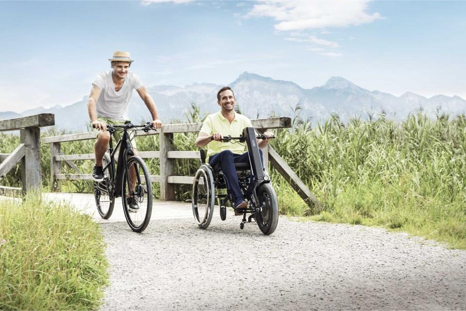 Mann im Rollstuhl mit e-pilot Zuggerät und Mann auf einem Fahrrad fahren durch hügelige Landschaft