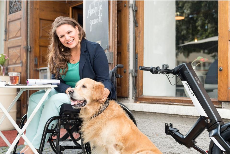 Frau mit abgedocktem e-pilot Zuggerät und Hund in Café.