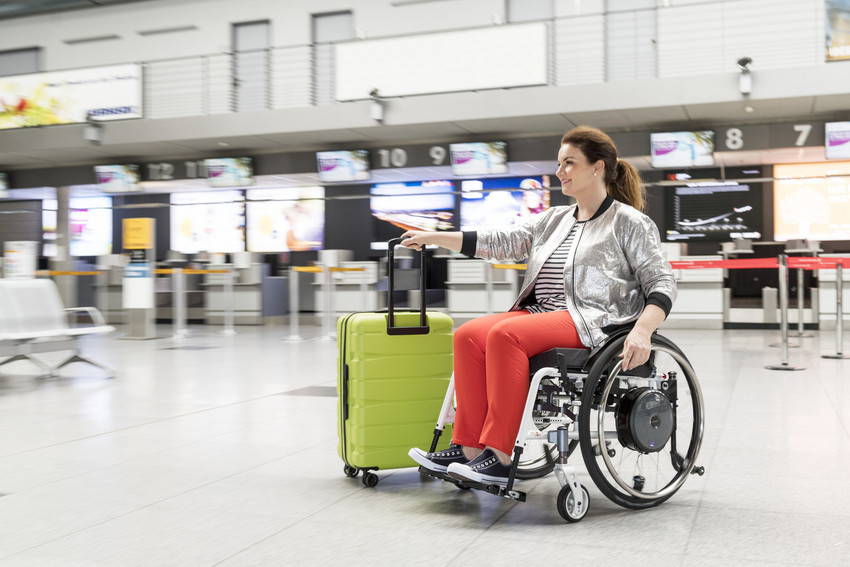 Rollstuhlfahrerin am Flughafen mit Gepäck